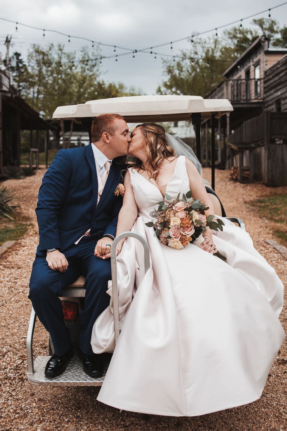 Newlyweds sharing romantic moments on rustic benches under string lights.