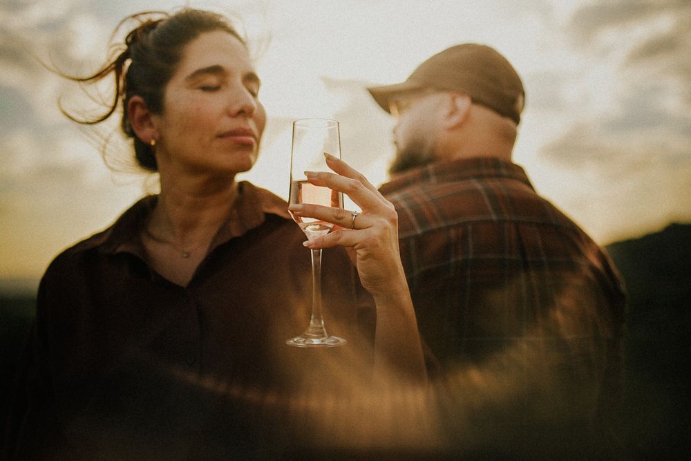 Couple toasting with champagne glasses at golden sunset, romantic outdoor celebration with warm light.