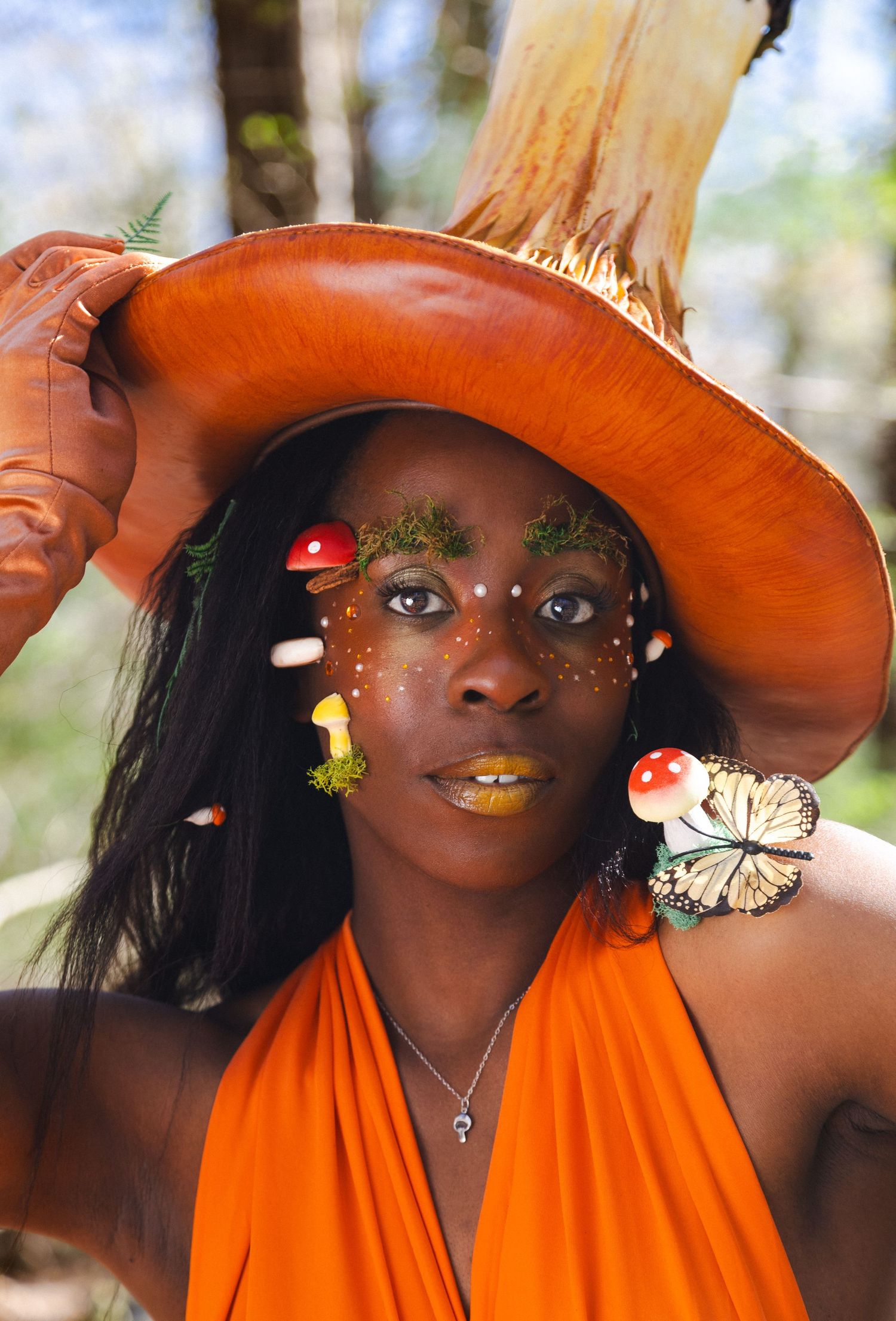 Creative portrait series with orange hat and butterfly decorations in natural outdoor setting.
