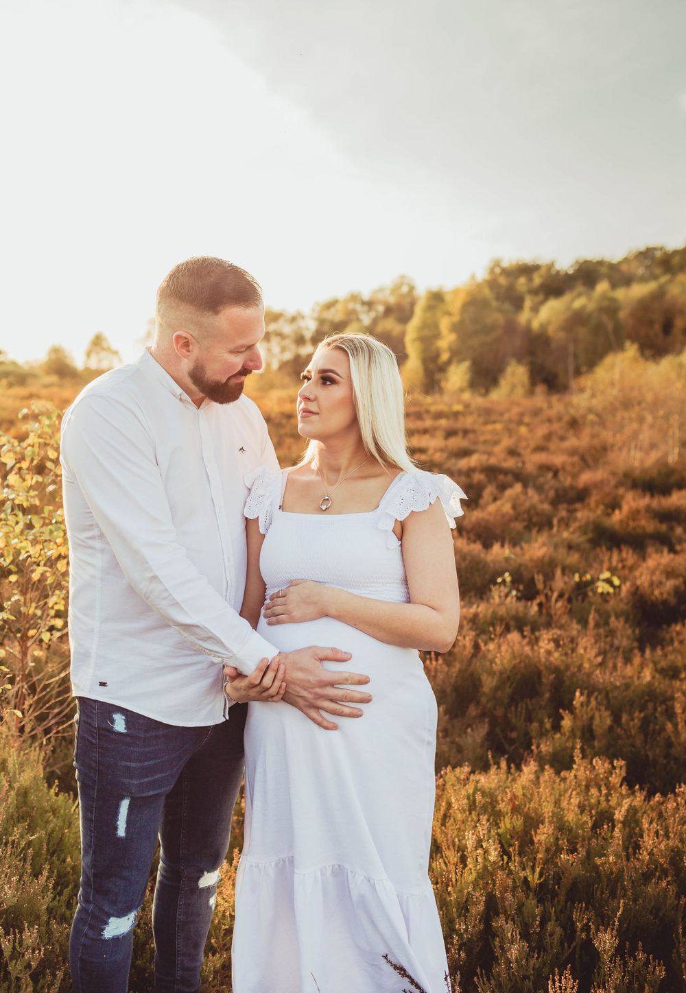 Couple embracing outdoors during sunset maternity photo session in natural setting.