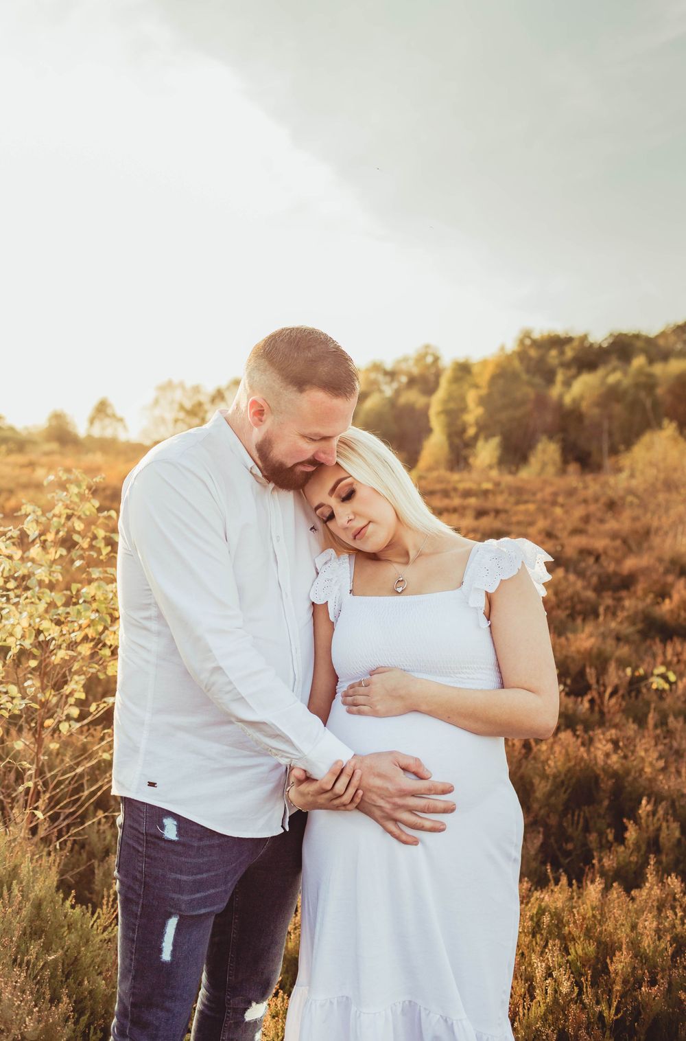 Intimate maternity photo of couple sharing tender moment in golden evening light.