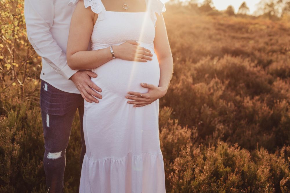 Couple in white clothing sharing intimate moment during outdoor maternity photoshoot.