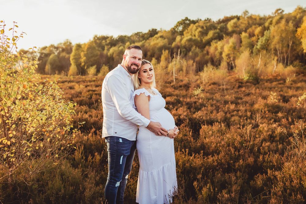 Couple embraces in a golden field during sunset maternity photoshoot.