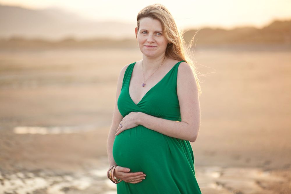 Woman in green dress standing on beach during golden hour.