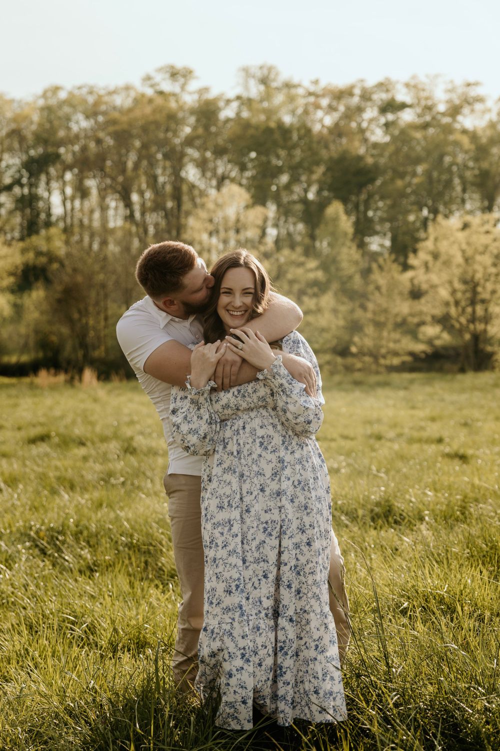 Intimate moment between couple sharing embrace in golden sunset meadow with floral dress and casual attire.