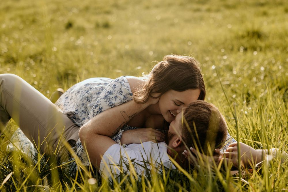 Tender moment captured between couple lying in tall grass during golden hour.