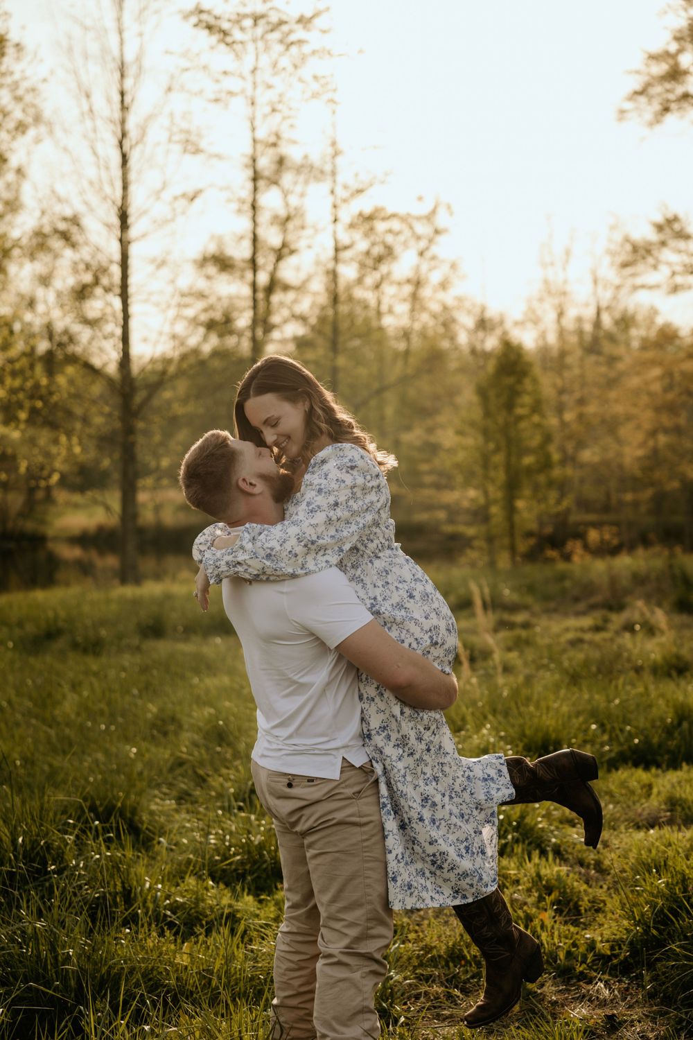 Joyful couple embracing in meadow with person in floral dress being lifted up.