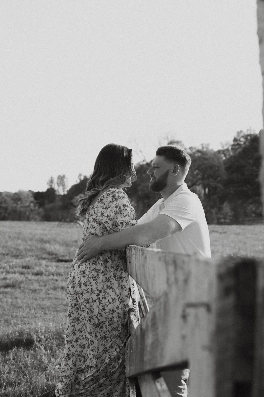 Black and white portrait of couple sharing tender moment by rustic fence.