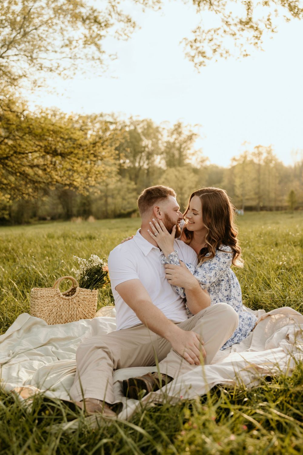 Couple sharing an intimate moment on a picnic blanket in a sunny meadow with a wicker basket nearby.