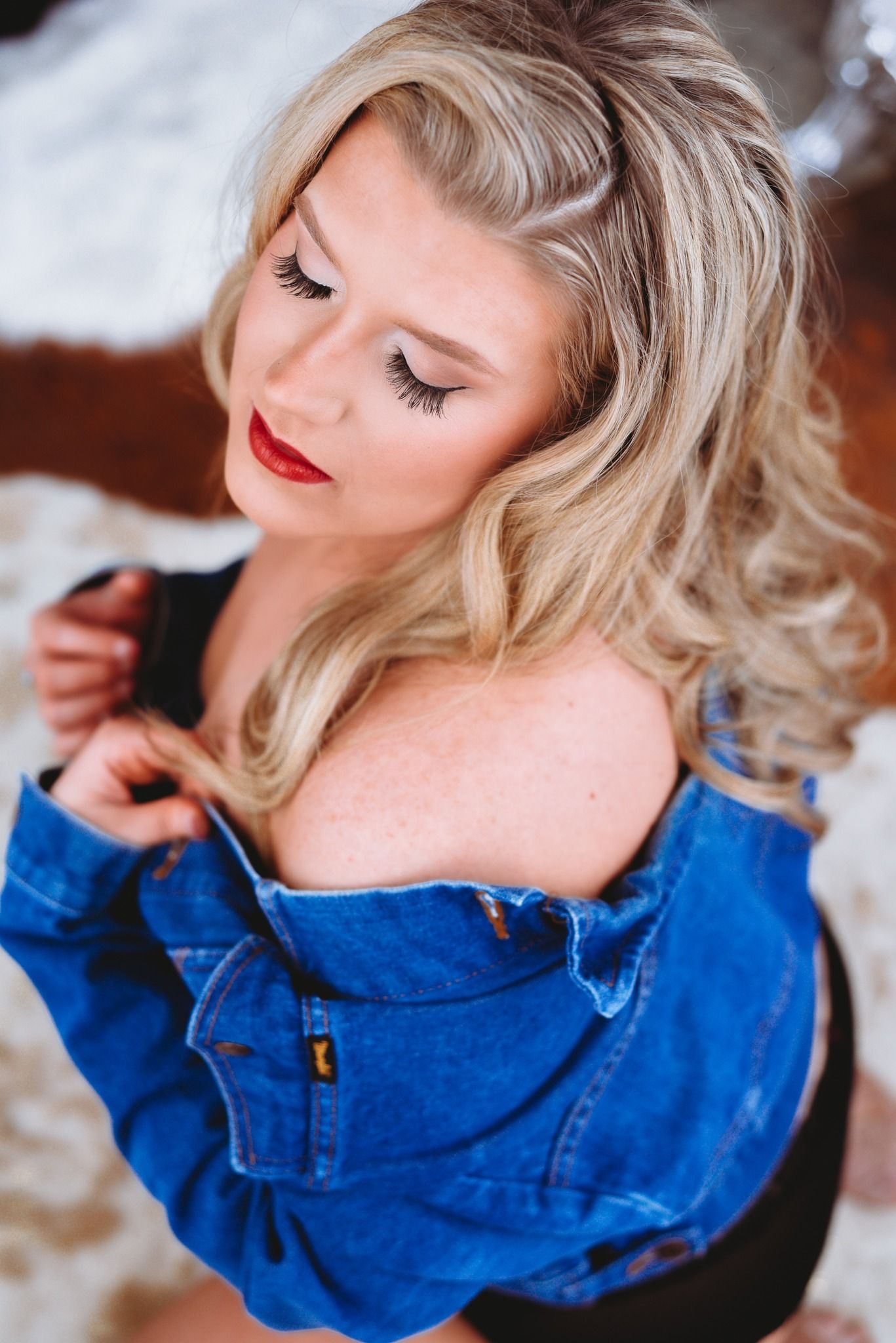 Stylish overhead portrait featuring wavy blonde hair, red lipstick, and an off-shoulder denim jacket.