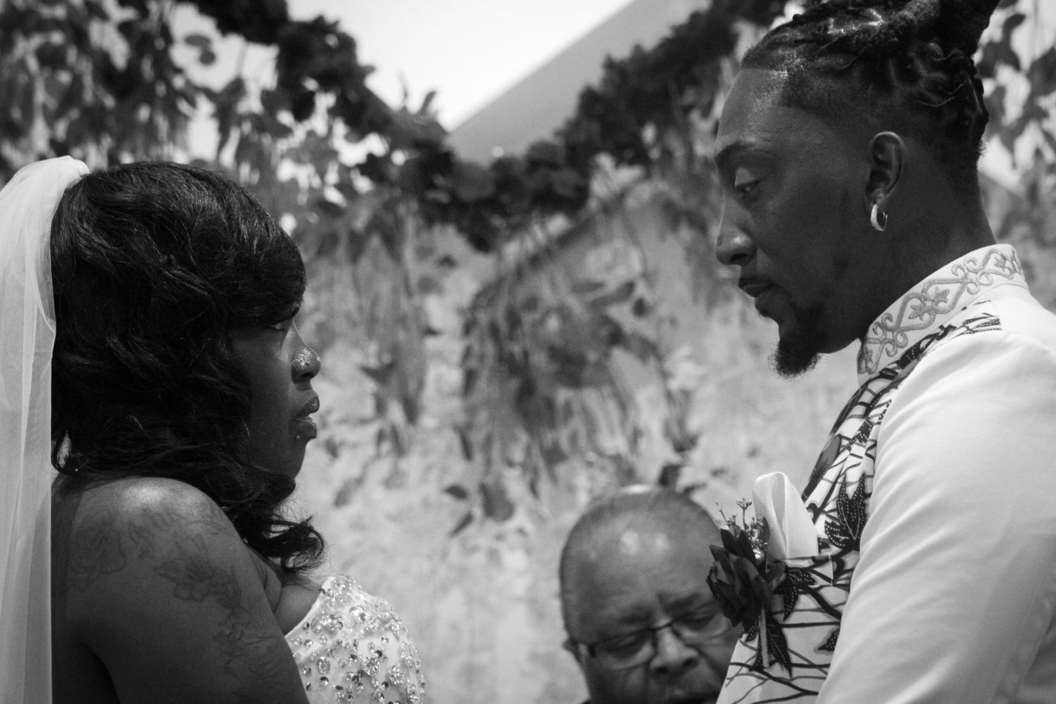 A black-and-white photo of the bride and groom exchanging vows during their wedding ceremony, capturing an emotional moment.