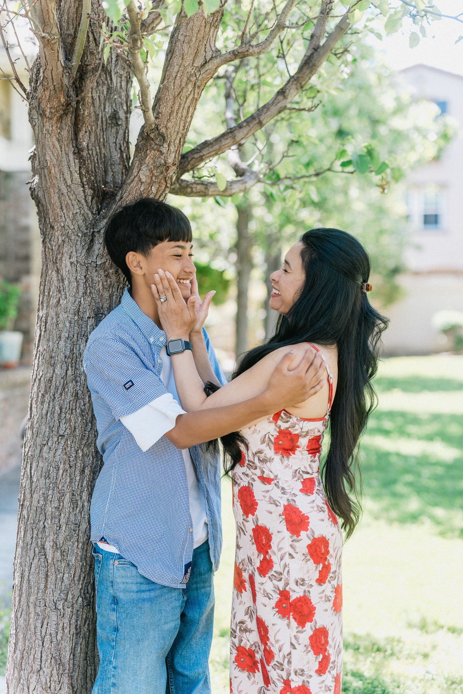 Couple shares a playful moment while posing by a tree on a sunny afternoon.