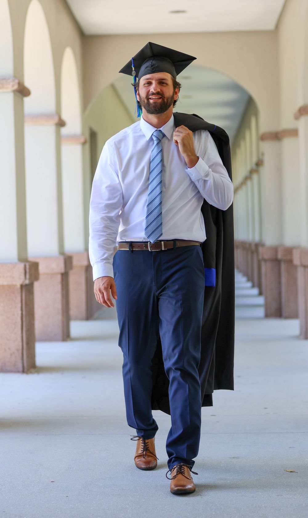 Graduate in cap and gown walks confidently through an arched hallway in formal attire Florida Gulf Coast University, Florida