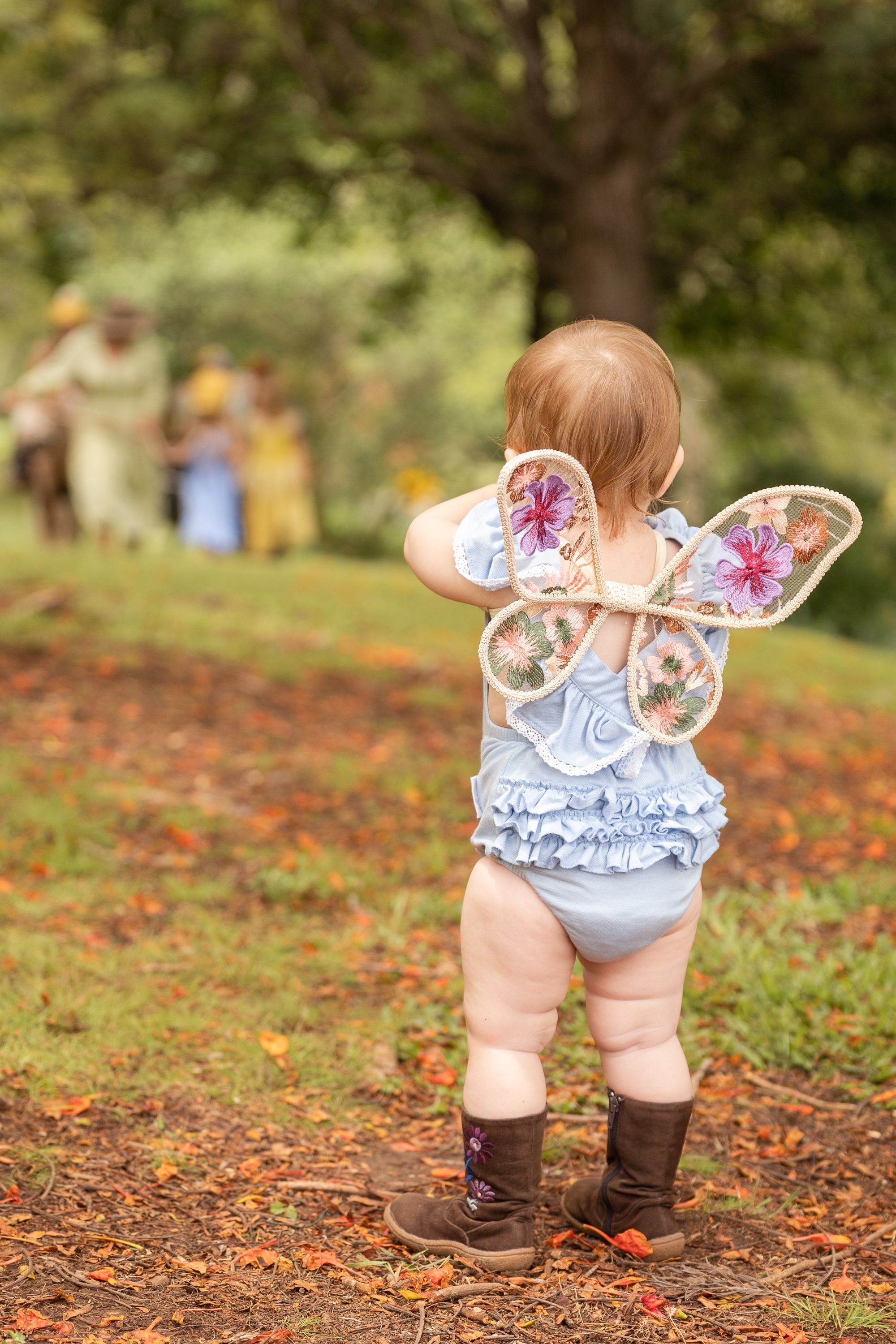 Small boots and ruffled bloomers shown from behind on an autumn ground covered in leaves.