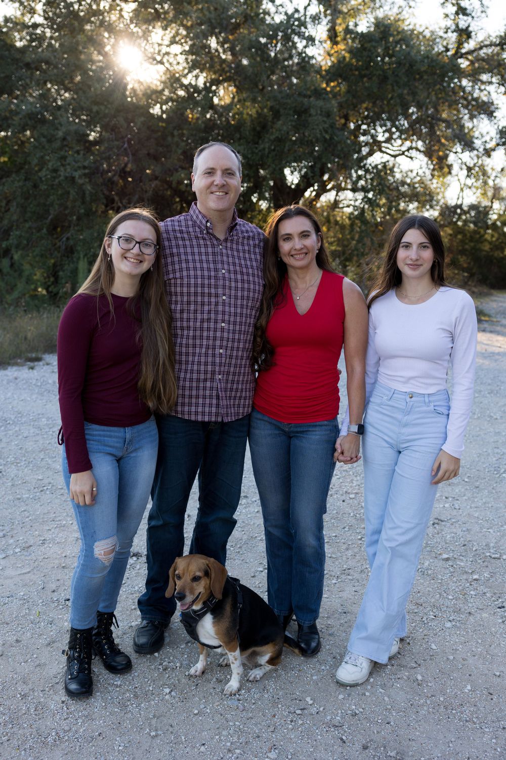 Family poses with their Beagle dog on gravel path during golden hour.