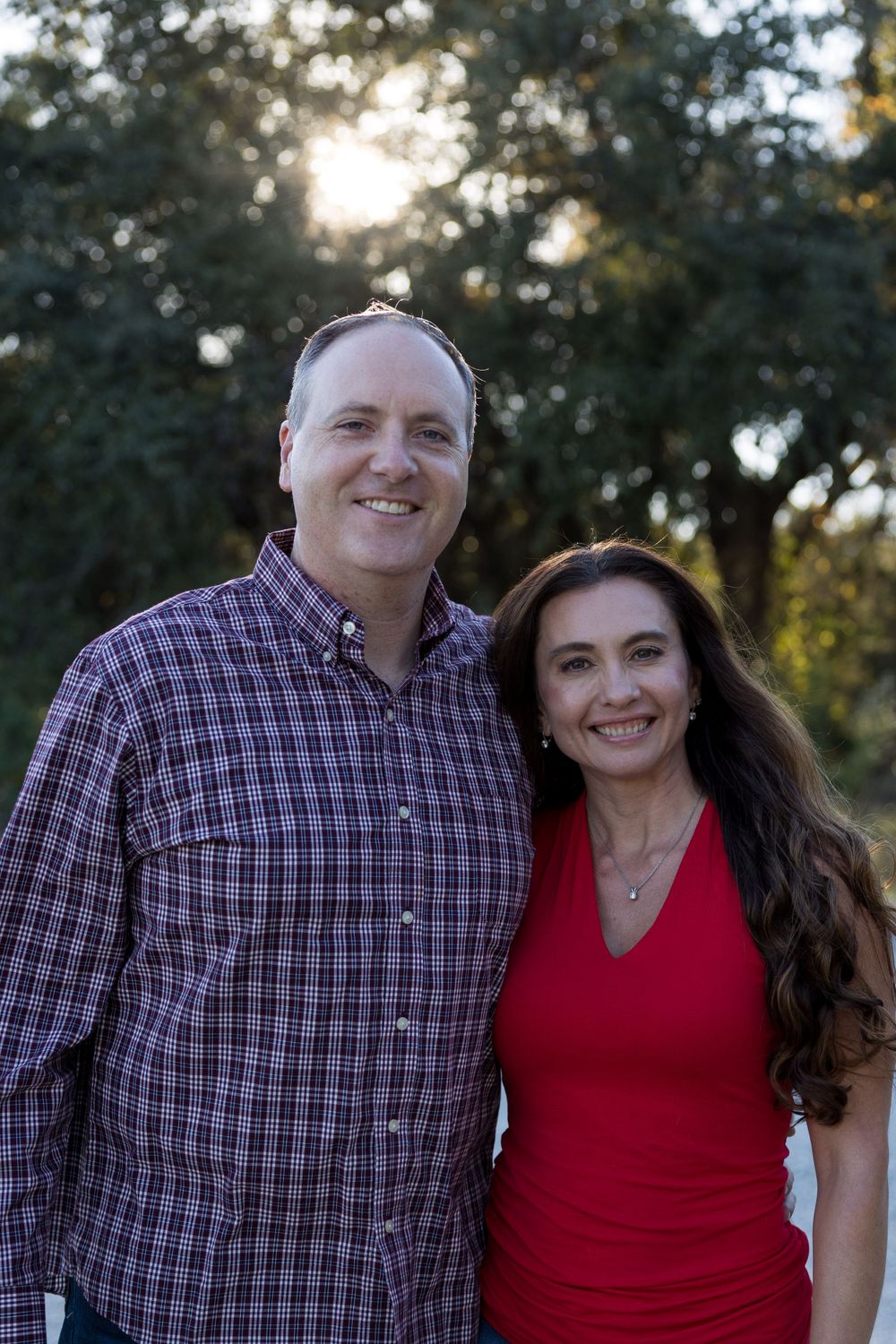 Couple in casual attire poses together outdoors during sunset.