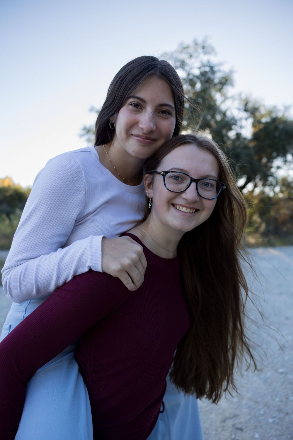 Two people share playful piggyback ride outdoors at dusk.