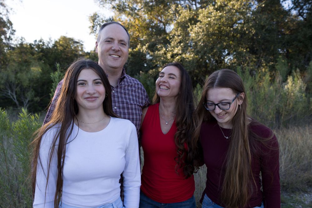 Happy family of four smiling together outdoors during golden hour.