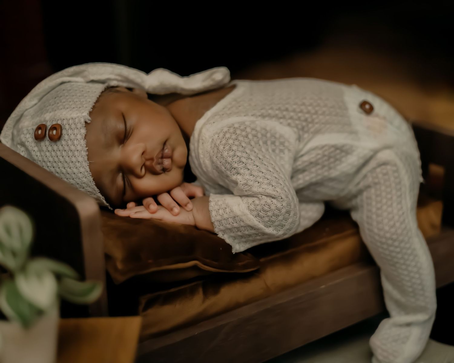 Peaceful newborn sleeping in white knit outfit on brown leather surface.