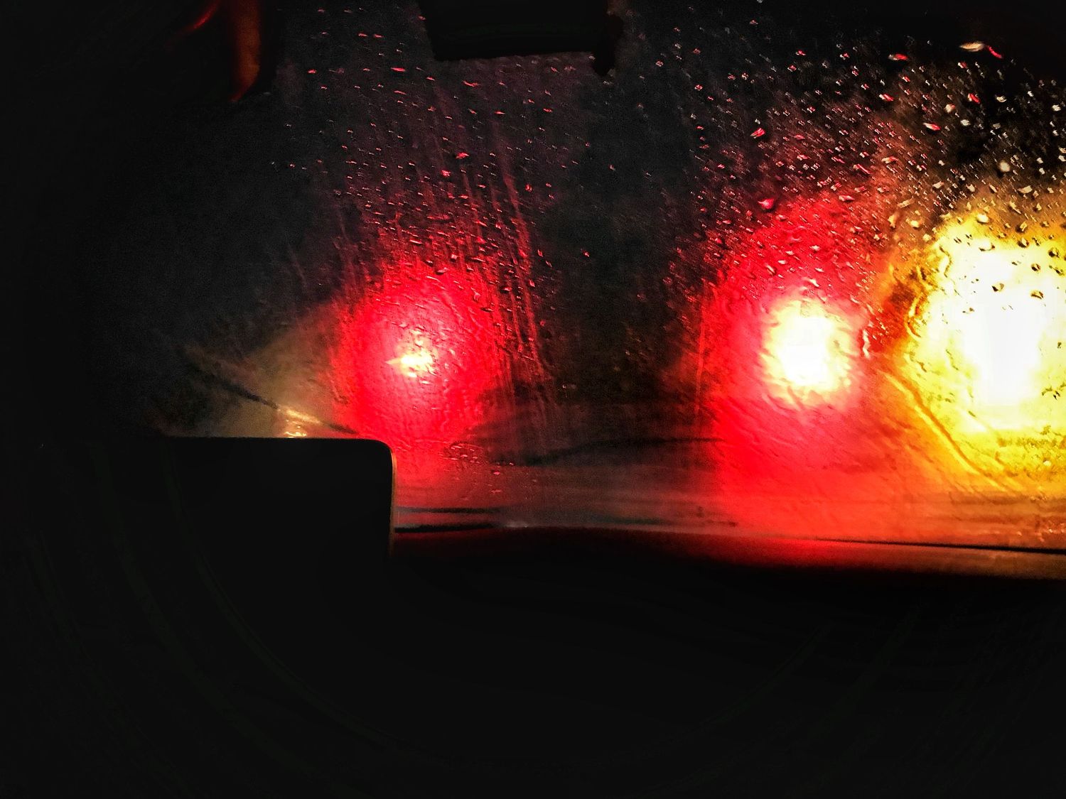 Blurry red and yellow lights visible through a rain-covered window at night.