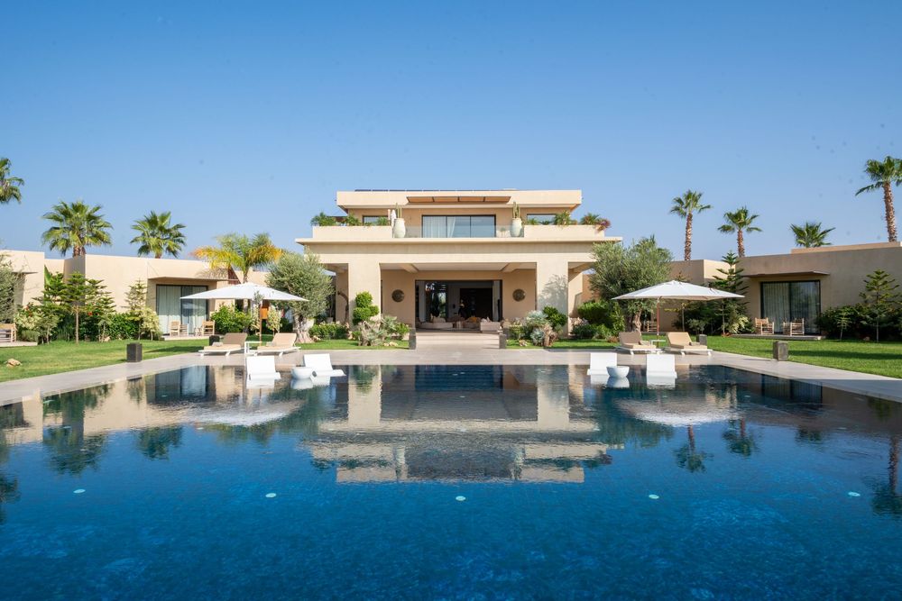 Modern luxury villa with infinity pool overlooking palm trees and desert landscape in panoramic view.