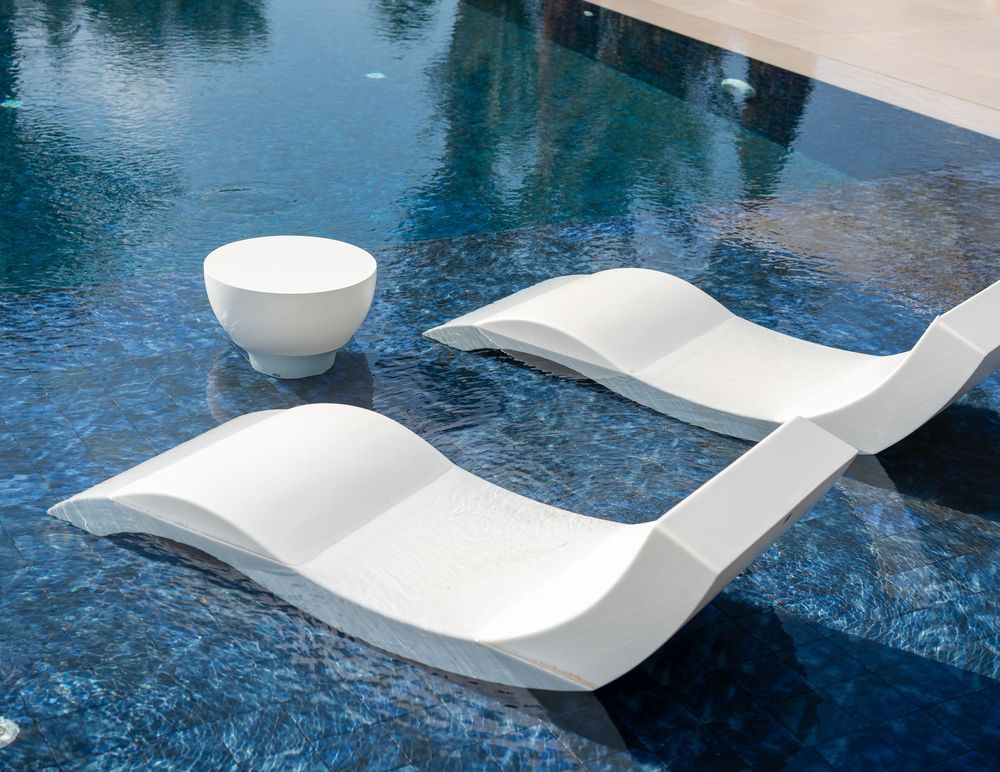 Sleek white curved lounge chairs line the edge of a tranquil blue swimming pool.