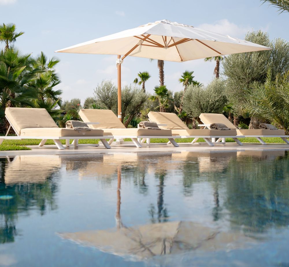 Luxurious infinity pool with white lounge chairs and umbrellas surrounded by palm trees and tropical landscaping.