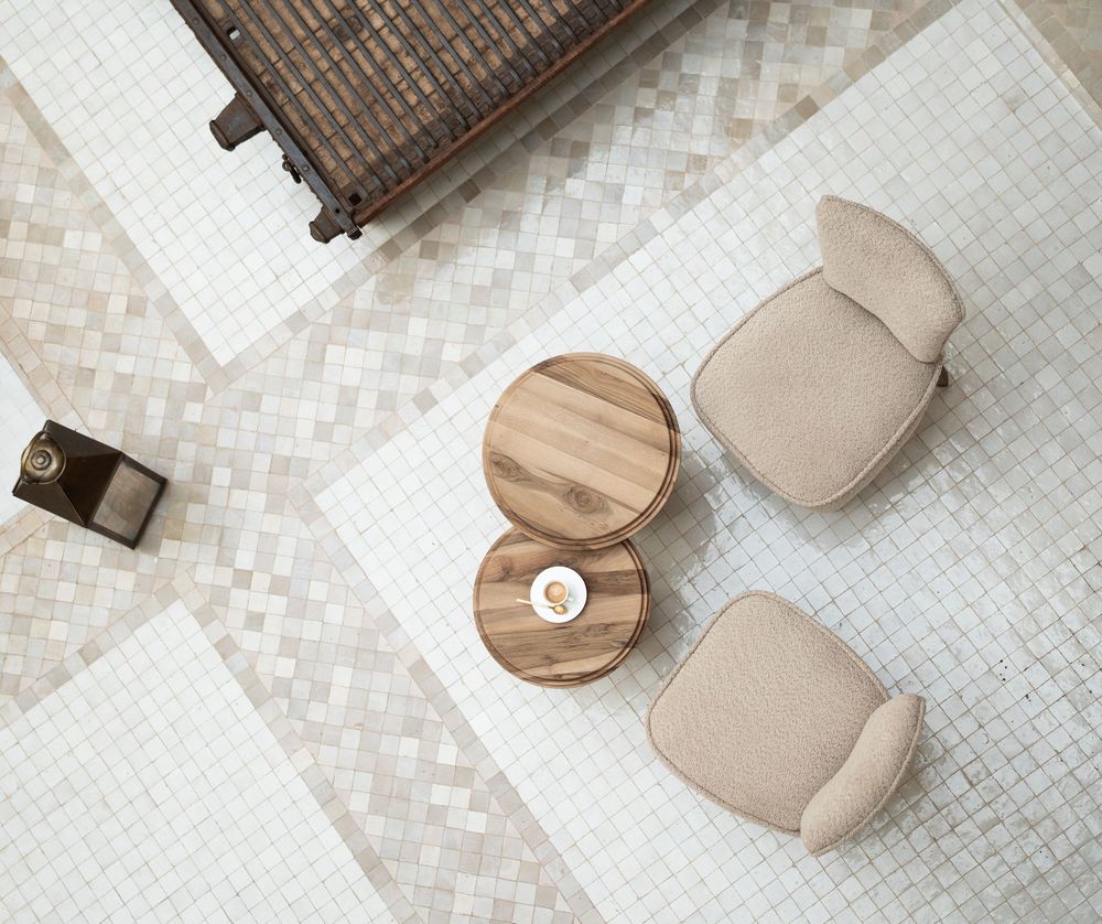 Wooden round coasters arranged on white mosaic tile surface with neutral beige tones and shadows.