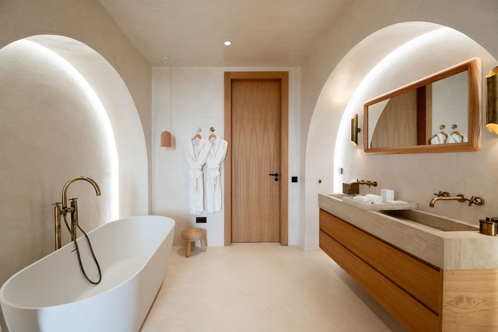 Modern luxury bathroom with curved archways, freestanding white bathtub, and floating wooden vanity with vessel sink.