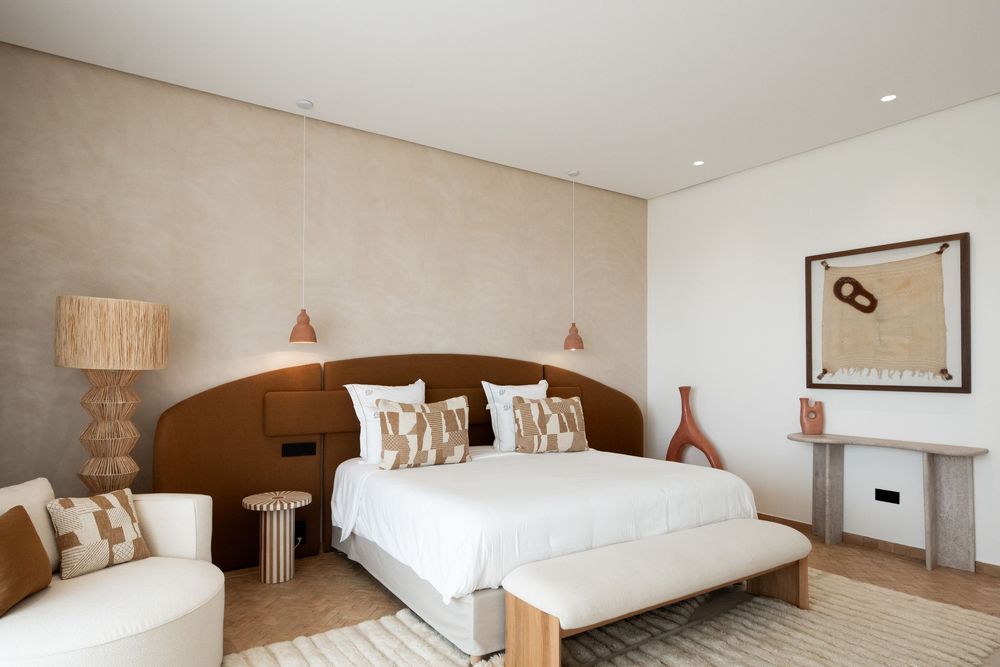 Modern minimalist hotel room with beige tones featuring a comfortable bed, sleek furnishings, and warm lighting.