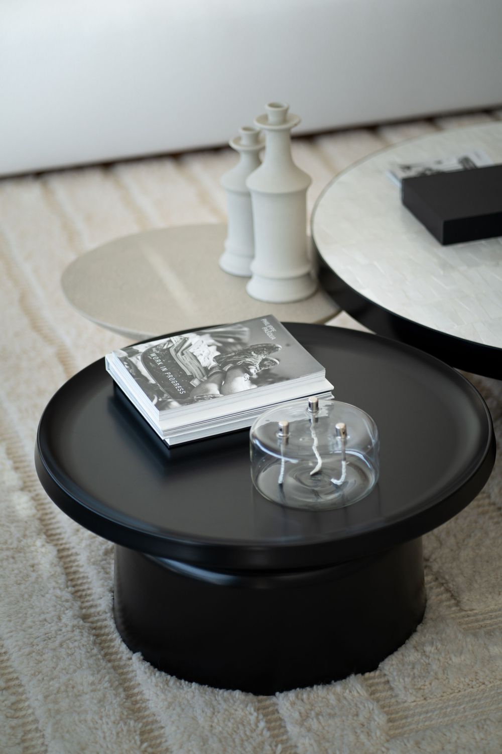 Minimalist black round coffee table with decorative objects and book on carpet.