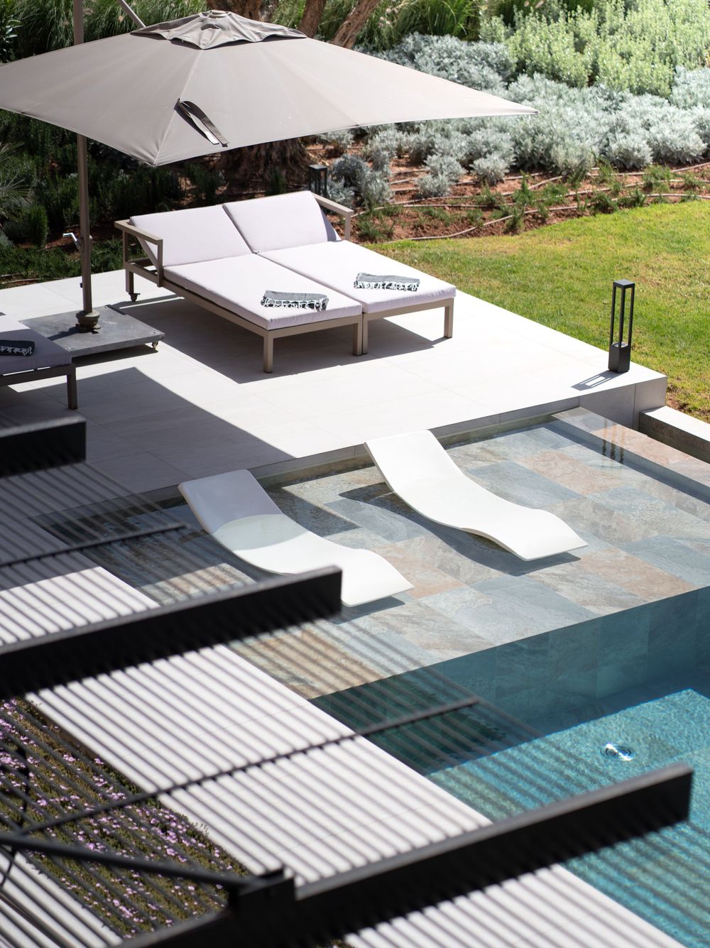 Modern pool deck with loungers and umbrella featuring stepped entry into turquoise water.
