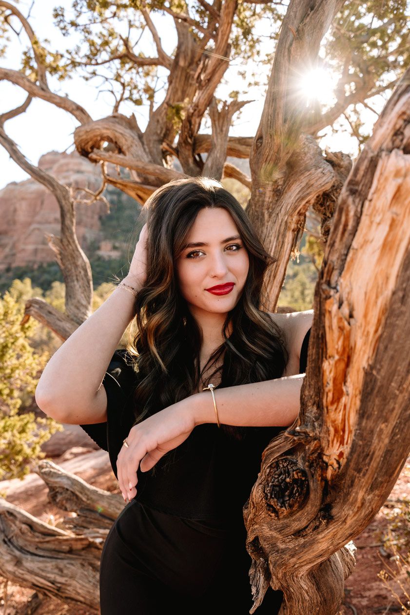 Sunlit portrait against gnarled tree branches with Sedona red rock formations in background.