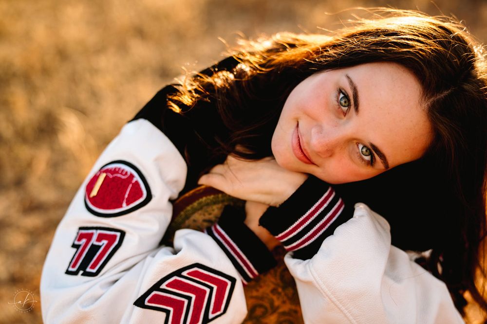 Outdoor portrait of person wearing varsity letterman jacket at sunset.