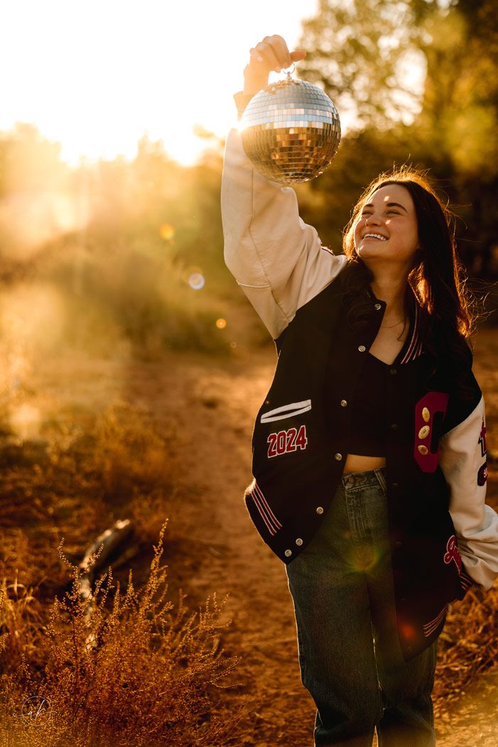 Person holding disco ball in varsity jacket against Sedona sunset desert backdrop.