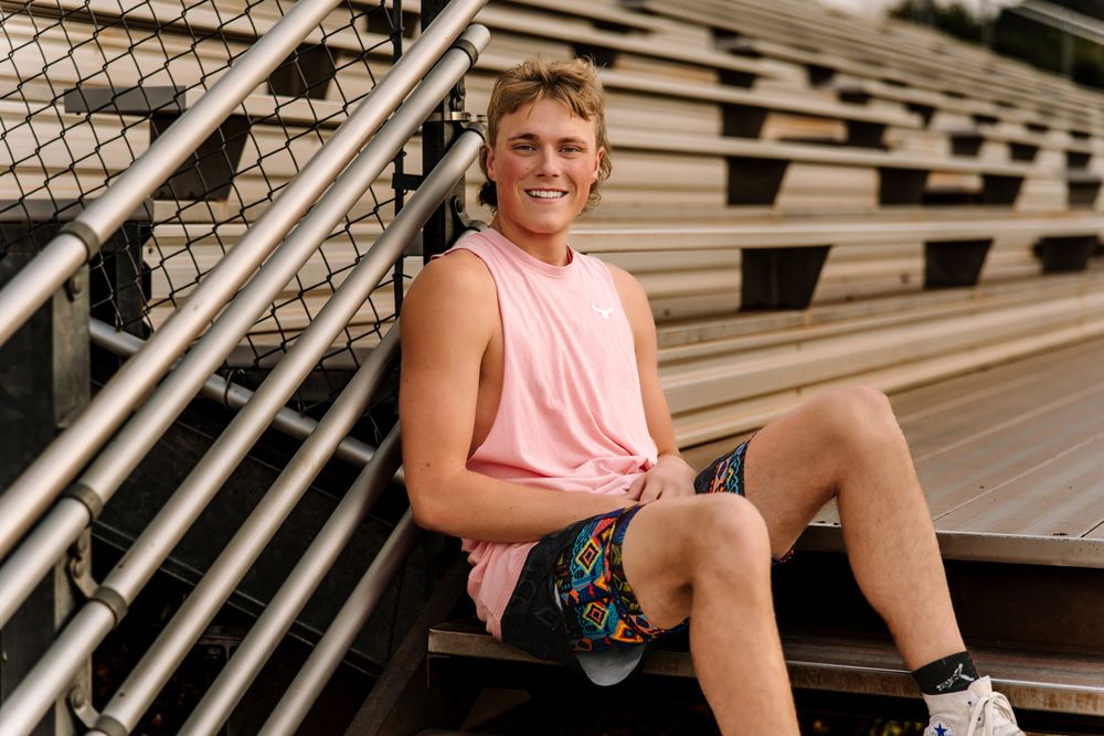 Athlete in pink tank top sits casually on stadium bleacher steps.