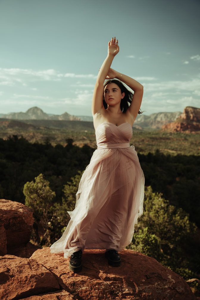 Woman in pink dress dancing on Sedona red rock formation during sunset.