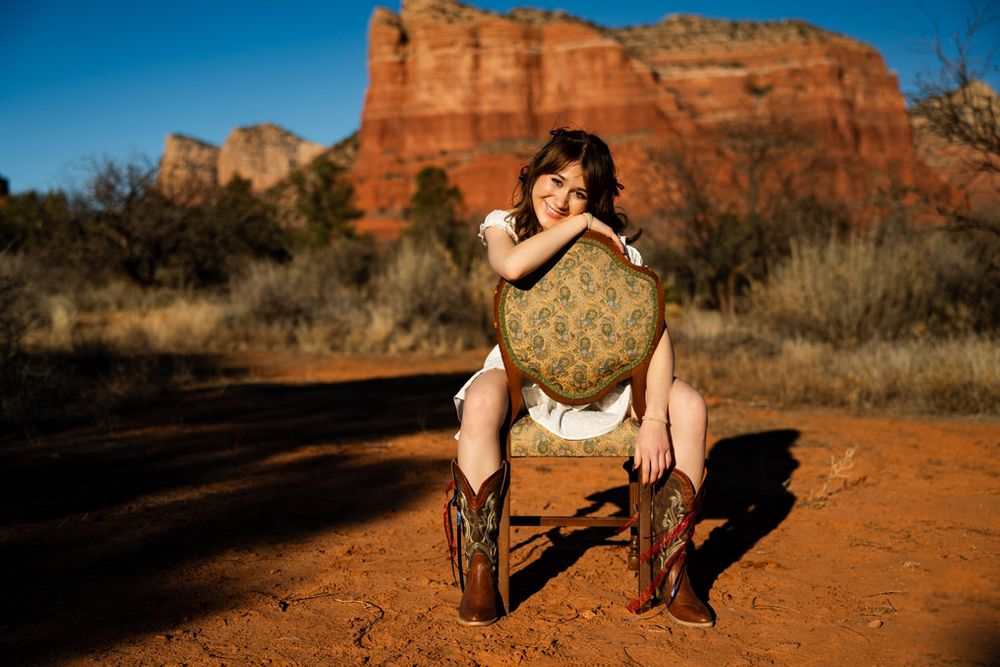 Person in boots sitting on rustic bench against Sedona red rock formations in desert setting.