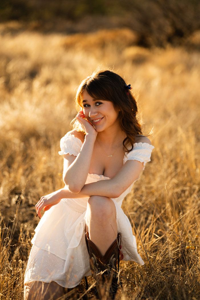 Someone in a white dress and boots poses playfully in a sunlit Sedona field.
