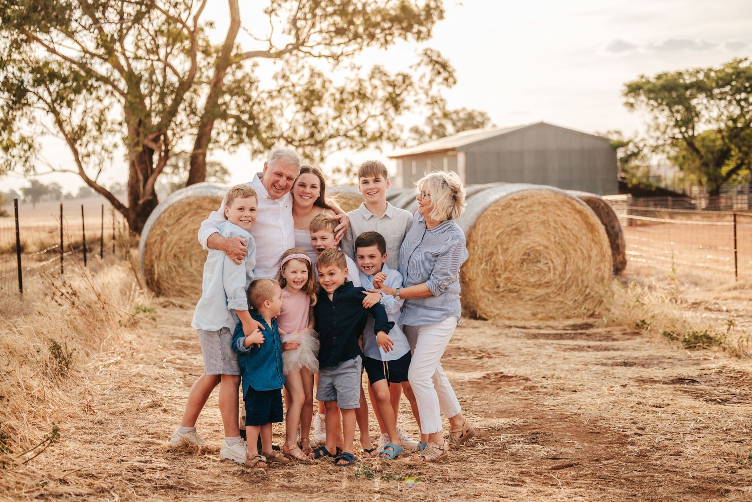 Extended family gathers for sunset portrait session near rustic hay bales in countryside setting.