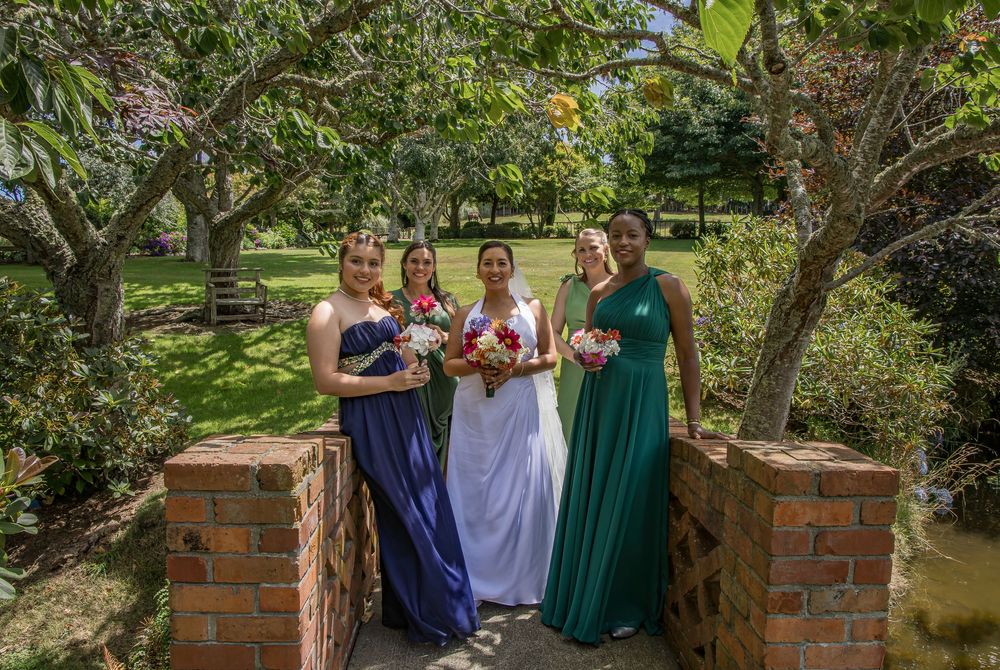 Bride in white gown with three bridesmaids in navy and green dresses holding bouquets in a garden setting.