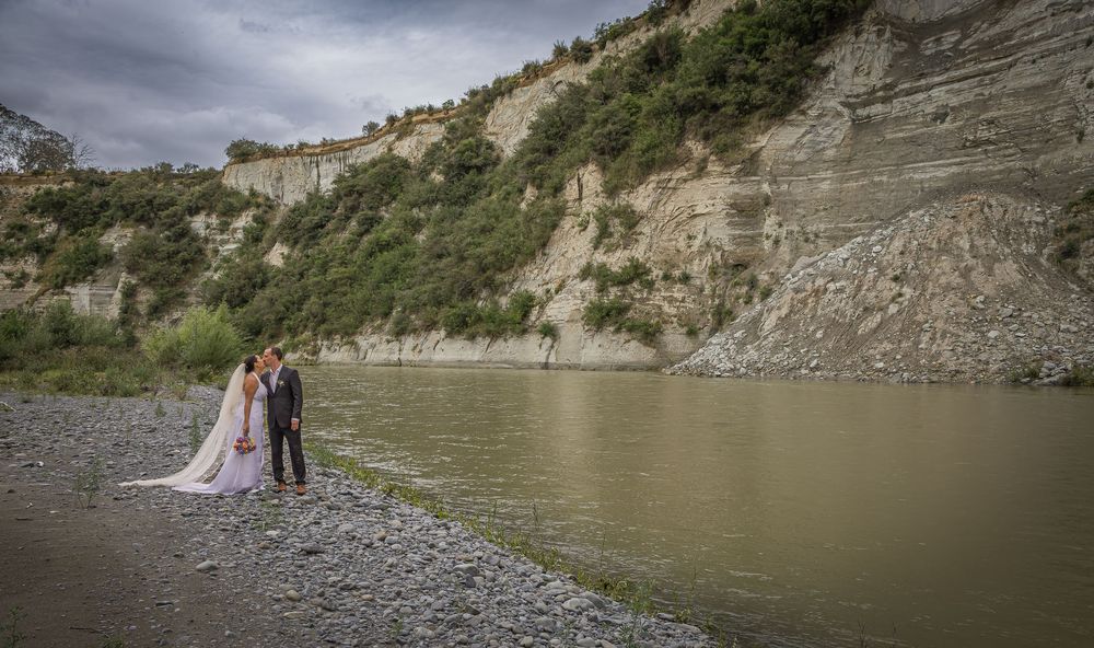 Bride and groom standing by a river with dramatic rocky cliffs in the background on their wedding day.