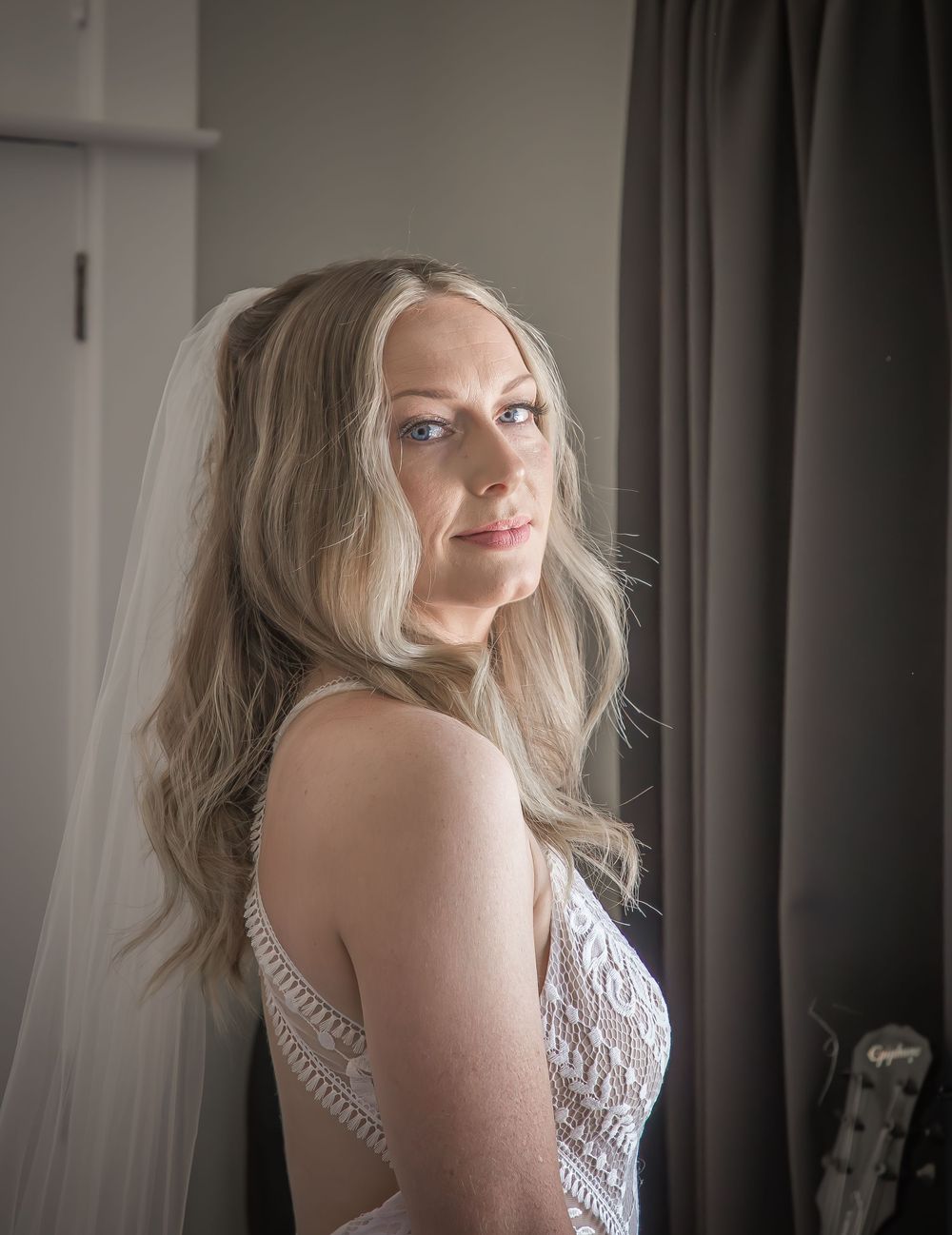 Side view portrait of someone with long wavy blonde hair wearing a white lace dress in soft window lighting.
