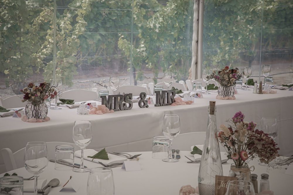 An elegant wedding reception table setting with Mrs & Mr signs and delicate flower centerpieces in a bright venue.