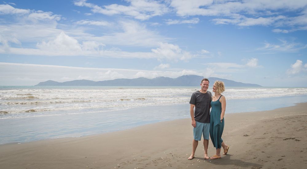 Couple walking together on a scenic beach with mountains and blue skies in the distance.
