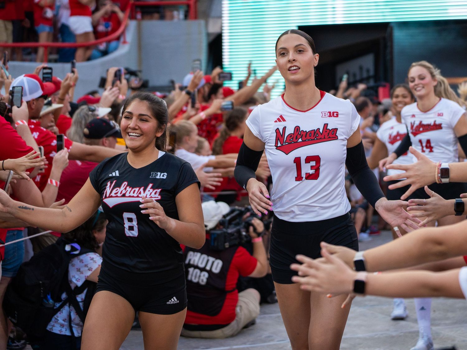 Athletes high-fiving fans during team entrance at volleyball game with crowd in red.