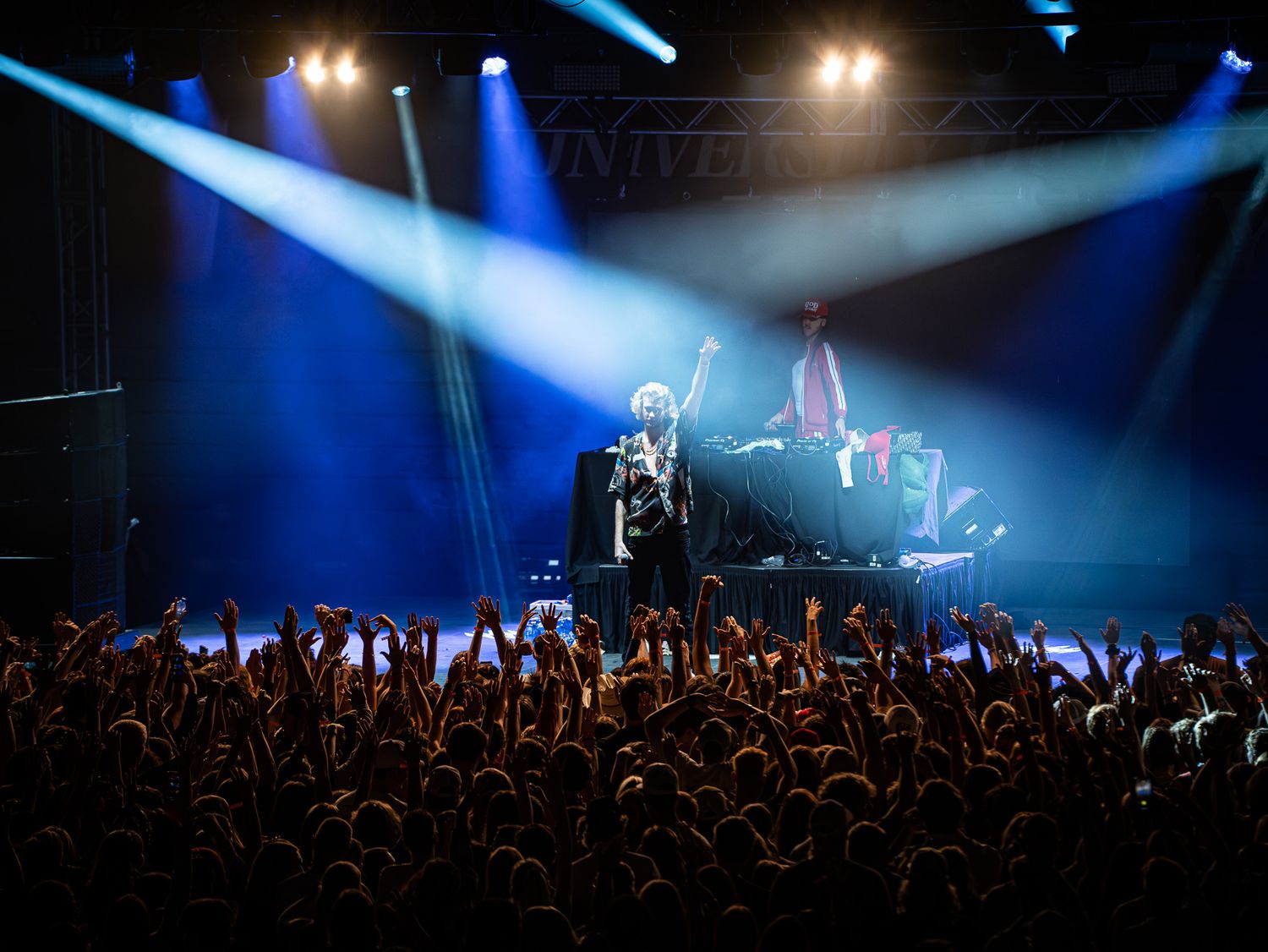 Concert crowd with raised hands under dramatic blue stage lighting.