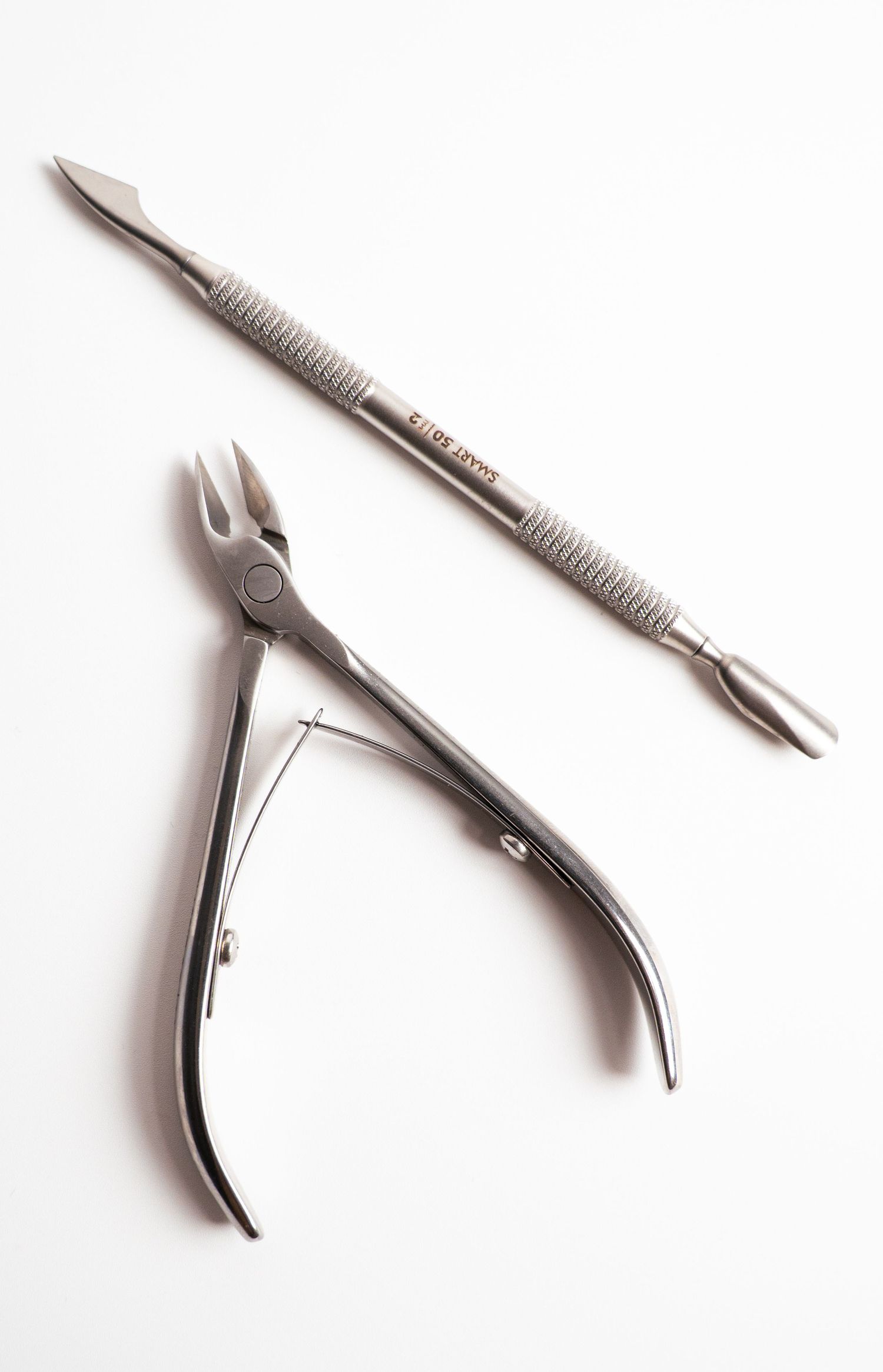 Professional manicure tools including nail clipper and cuticle pusher on white background.