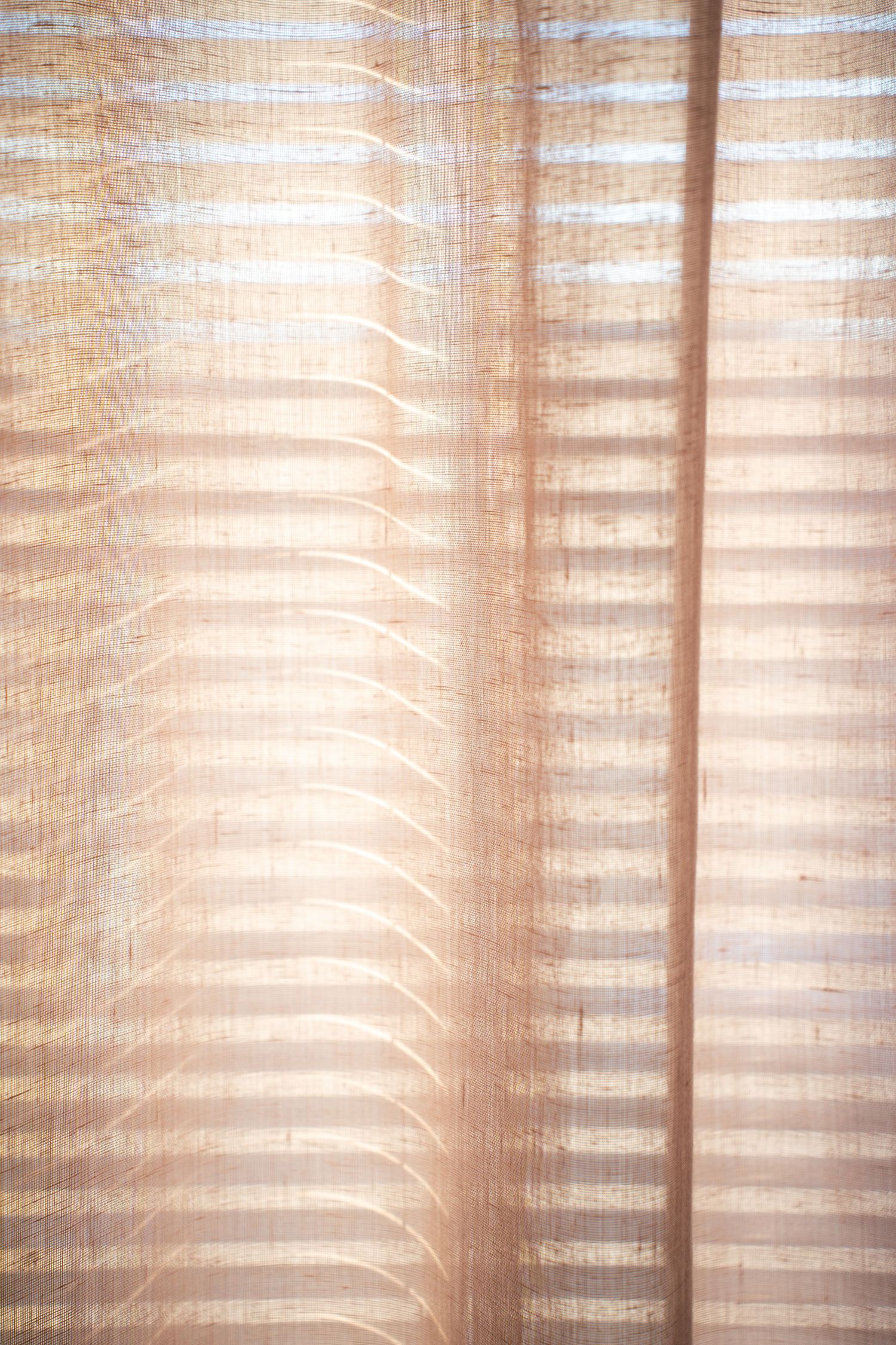 Sunlight filtering through sheer curtains creating soft horizontal stripes and shadows.