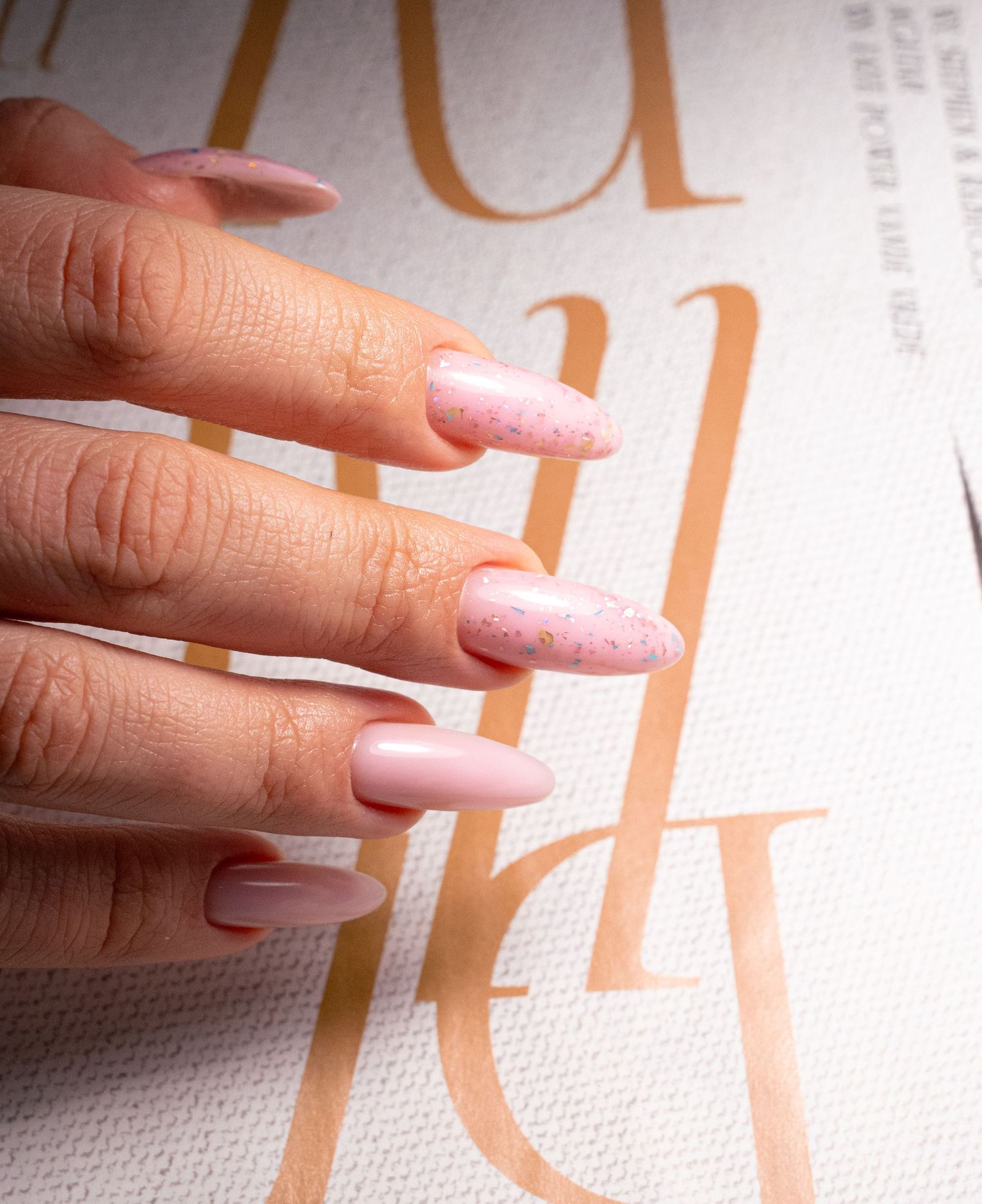 Manicured nails with pink gradient design photographed against typography background.